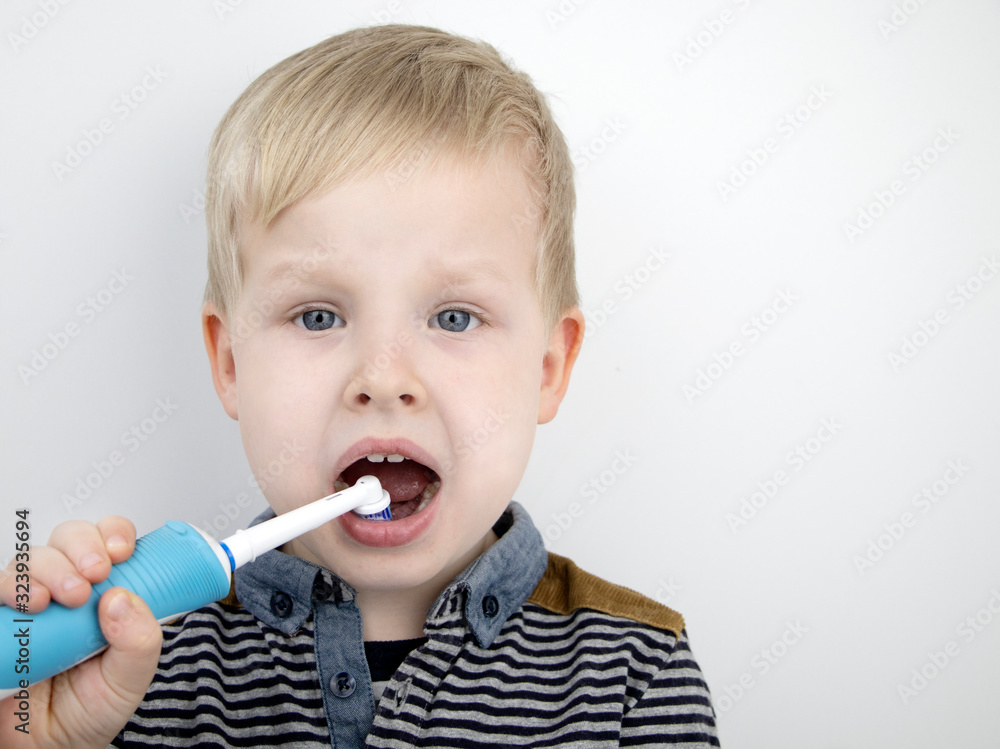 Four year old child brushes his teeth with an electric brush. The boy on a white background laughs and holds a toothbrush. The concept of baby teeth and oral hygiene Four year old child brushes his teeth with an electric brush. The boy on a white background laughs and holds a toothbrush. The concept of baby teeth and oral hygiene