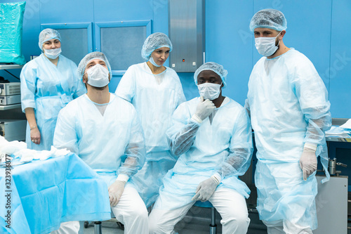 A team of doctors in uniform and medical masks rests after completion of a surgical operation