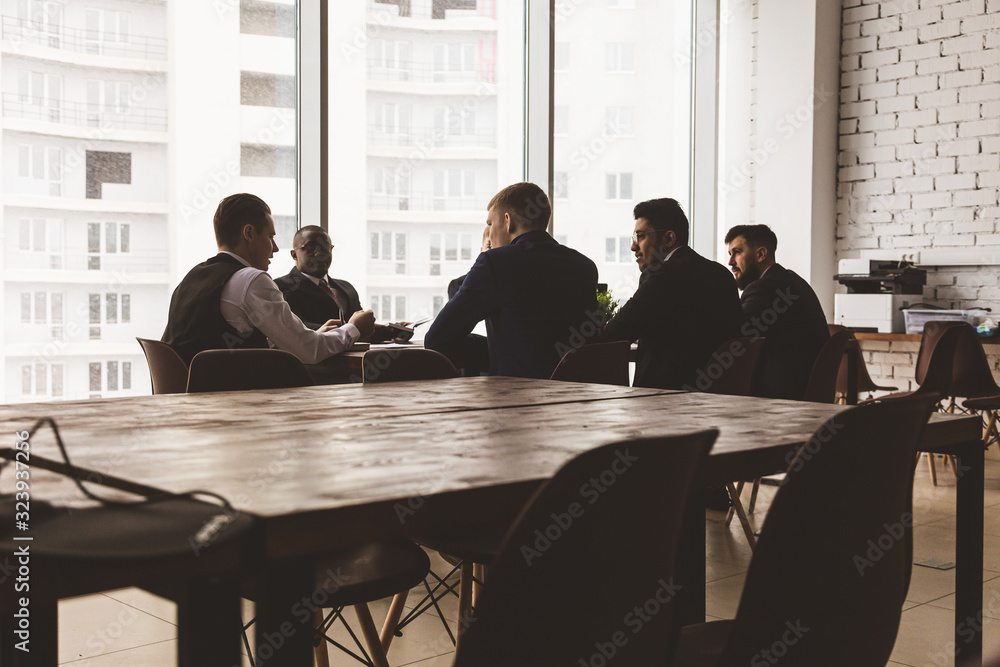 Silhouettes of people sitting at the table. A team of young businessmen working and communicating together in an office. Corporate businessteam and manager in a meeting. Silhouettes of people sitting at the table. A team of young businessmen working and communicating together in an office. Corporate businessteam and manager in a meeting.