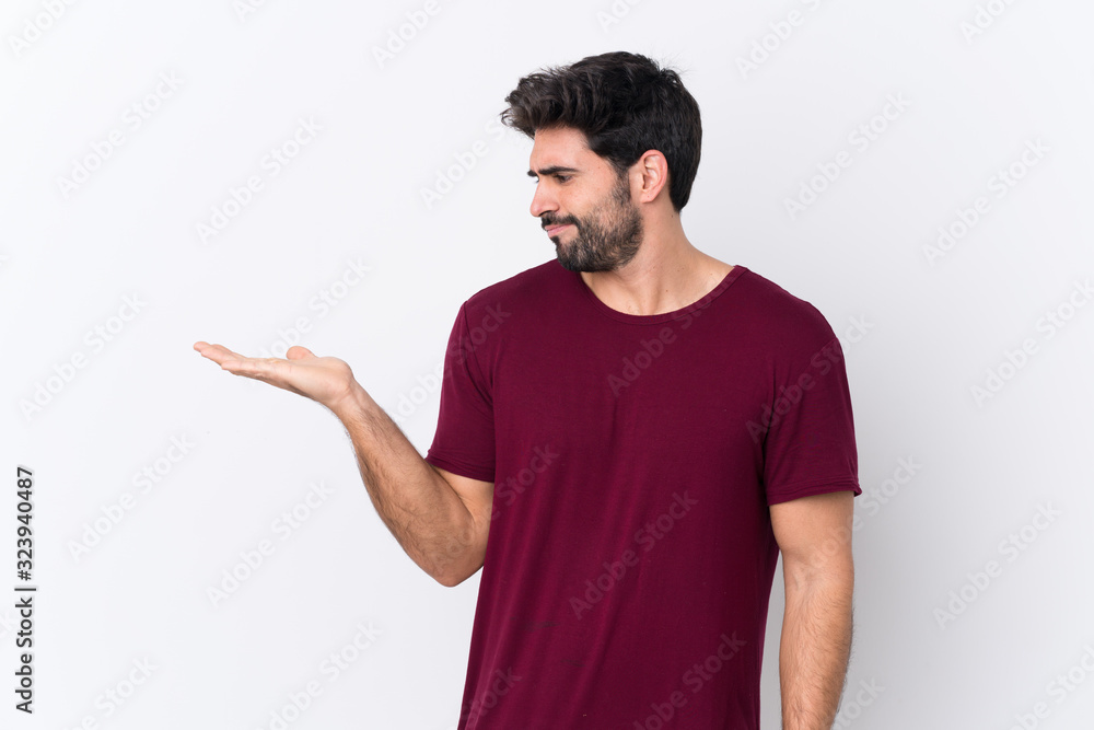 Young handsome man with beard over isolated white background holding copyspace with doubts Young handsome man with beard over isolated white background holding copyspace with doubts