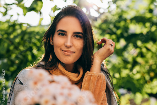 Close-up image of happy young woman with a bouquet of pink flowers on sunny day in the park. Pretty female recieved a gift a bouquet of flowers from her boyfreind in the city street. Woman's day photo