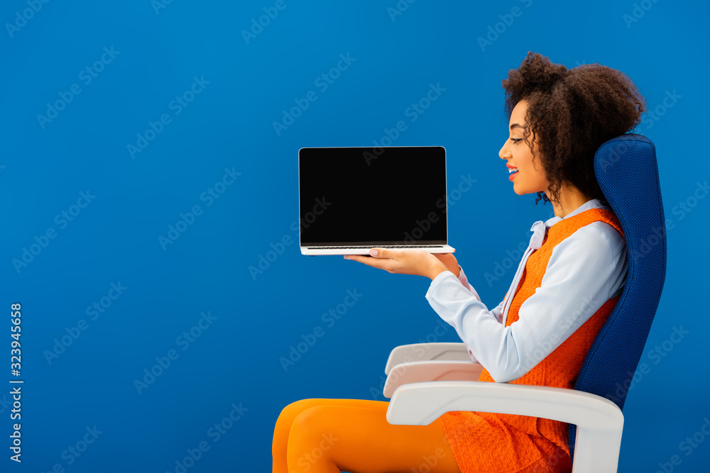 custom made wallpaper toronto digitalside view of smiling african american sitting on seat and holding laptop isolated on blue