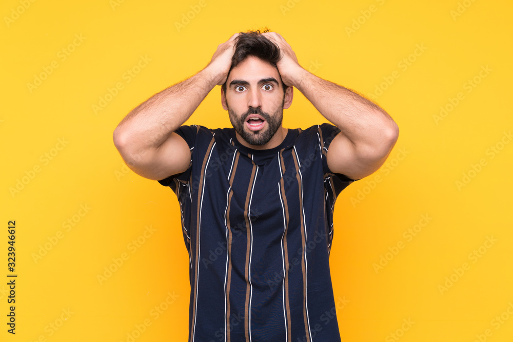 Young handsome man with beard over isolated yellow background with surprise facial expression Young handsome man with beard over isolated yellow background with surprise facial expression