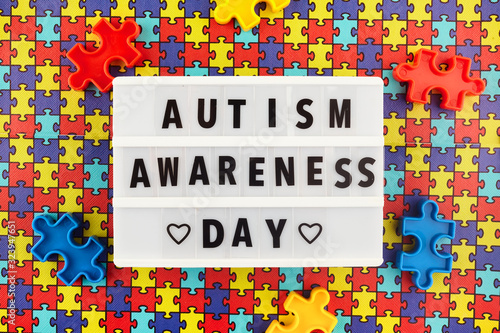 Light box with World autism awareness day text on colored puzzle background. Top view