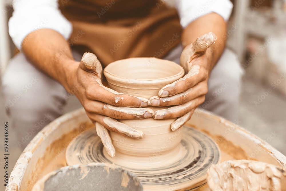 A young male potter works in his workshop on a potter's wheel and makes clay products. Close-up of hands