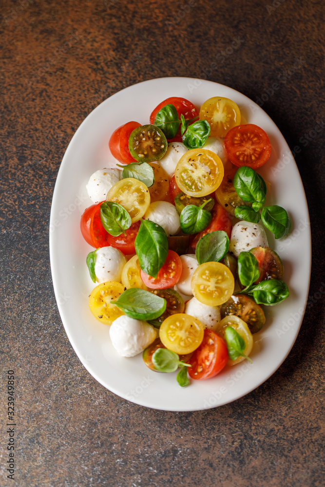 Italian caprese salad with sliced tomatoes, mozzarella cheese, basil, olive oil in wooden bowl. Italian food Italian caprese salad with sliced tomatoes, mozzarella cheese, basil, olive oil in wooden bowl. Italian food