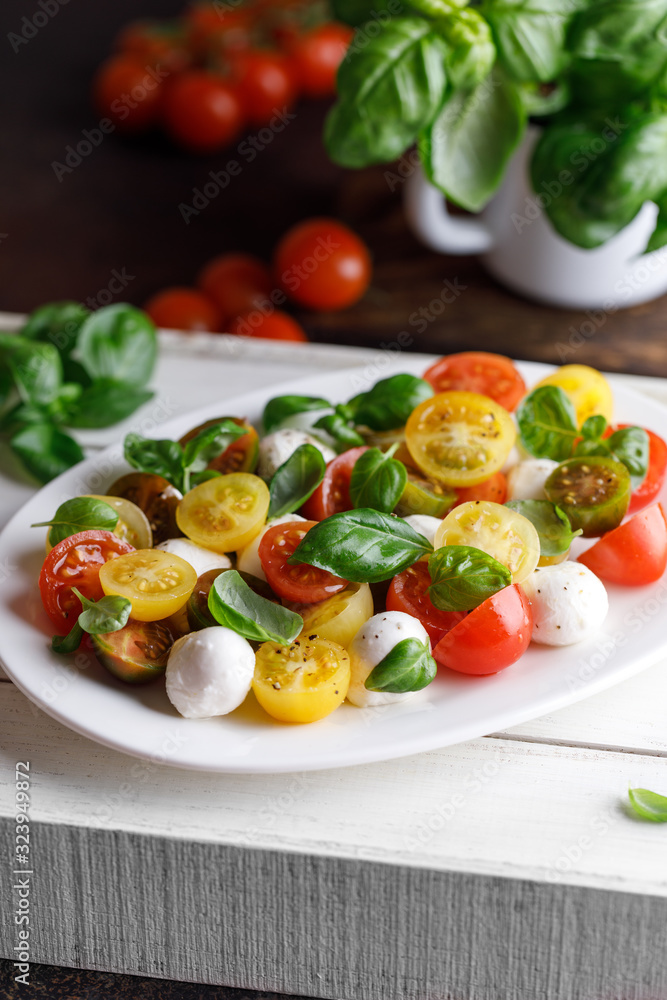 Italian caprese salad with sliced tomatoes, mozzarella cheese, basil, olive oil in wooden bowl. Italian food