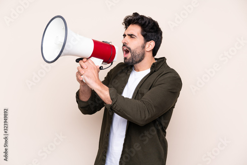 Young handsome man with beard over isolated background shouting through a megaphone