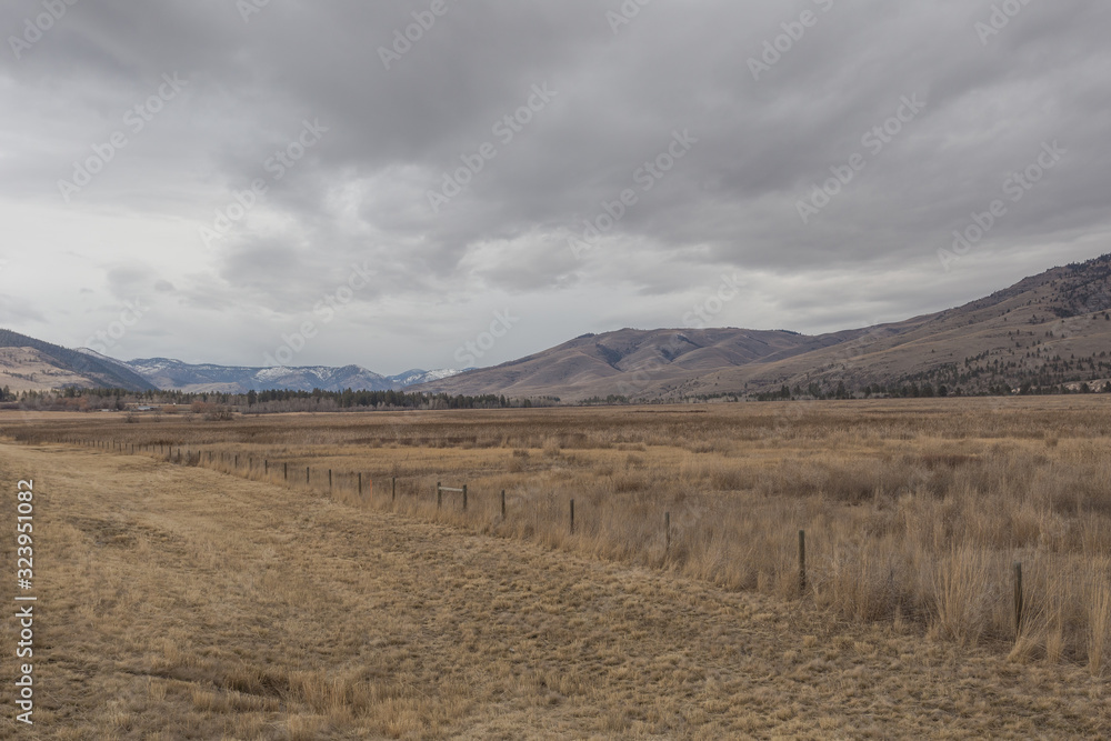 Vast open fields with cattle fencing in front of large rolling hill mountains