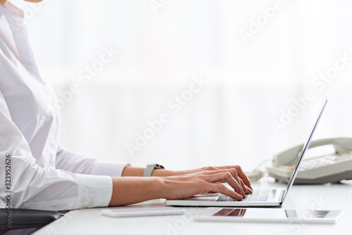 Cropped view of businesswoman using laptop near gadgets on table