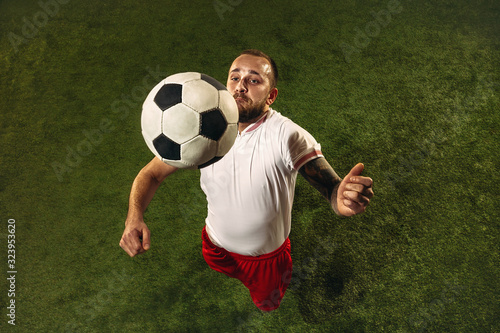 Top view of caucasian football or soccer player on green background of grass. Young male sportive model training, practicing. Kicking ball, attacking, catching. Concept of sport, competition, winning.