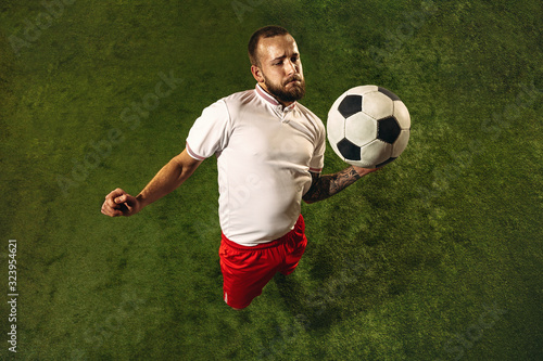 Top view of caucasian football or soccer player on green background of grass. Young male sportive model training, practicing. Kicking ball, attacking, catching. Concept of sport, competition, winning.