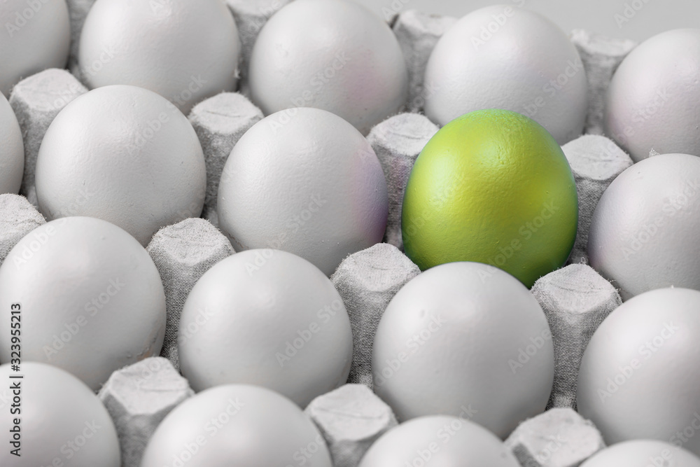 yellow-green, gold-tinged Easter egg in a box with identical white eggs, group, difference. symbol of individuality. concept for Easter. yellow-green, gold-tinged Easter egg in a box with identical white eggs, group, difference. symbol of individuality. concept for Easter.
