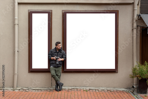 Young photographer stands in front of an empty billboard while taking pictures on the street