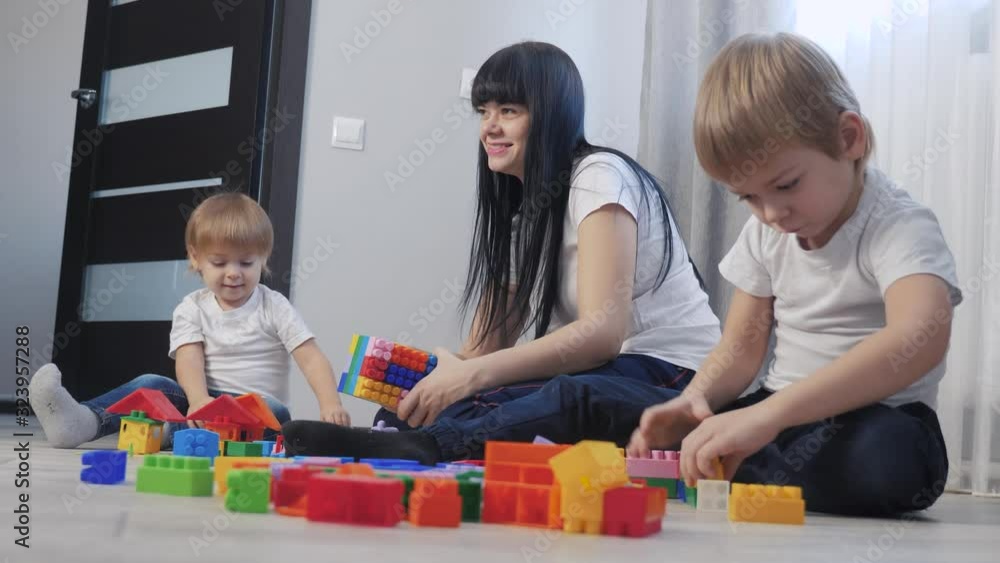 childhood happy family mom and children are playing concept little girl and boy brother and sister collects constructor teamwork. child plays toys sitting floor. children play in team toys on floor childhood happy family mom and children are playing concept little girl and boy brother and sister collects constructor teamwork. child plays toys sitting floor. children play in team toys on floor