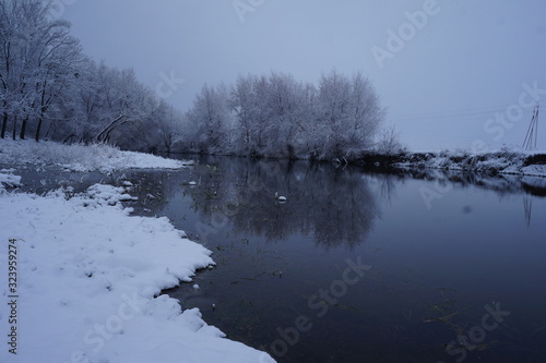 River in winter and tree branches covered with white frost.