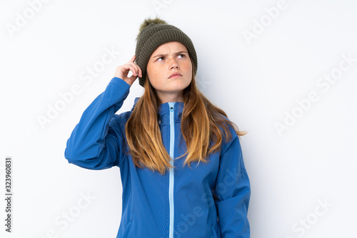 Ukrainian teenager girl with winter hat over isolated white background having doubts and with confuse face expression