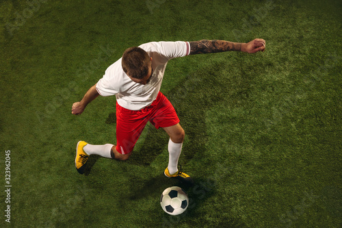 Top view of caucasian football or soccer player on green background of grass. Young male sportive model training, practicing. Kicking ball, attacking, catching. Concept of sport, competition, winning. © master1305