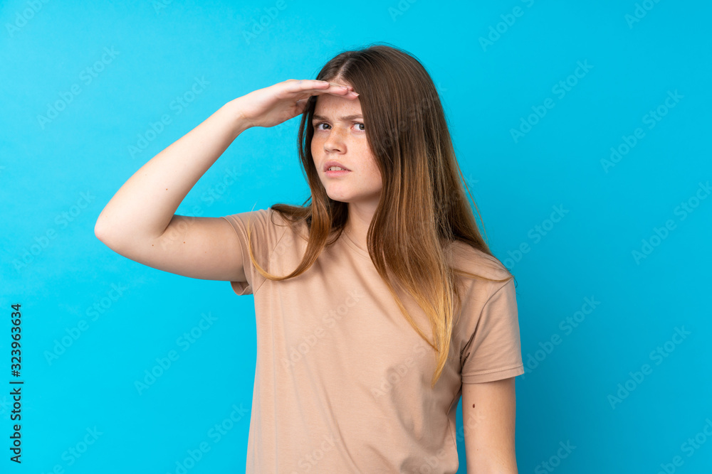 Ukrainian teenager girl over isolated blue background looking far away with hand to look something