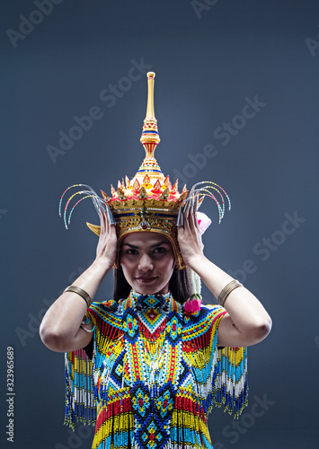 Young lady wearing Thai Tradition southern costume,made from colorful beads,raise hands touch Headdress,showing basic pattern folk dance,in front of solid backdrop. photo