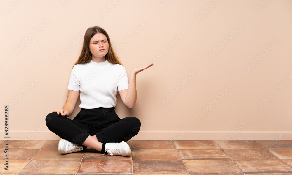 Ukrainian teenager girl sitting on the floor holding copyspace with doubts Ukrainian teenager girl sitting on the floor holding copyspace with doubts