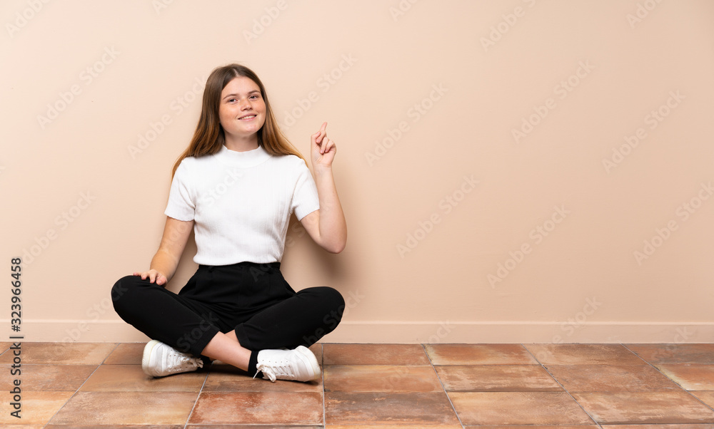 Ukrainian teenager girl sitting on the floor showing and lifting a finger in sign of the best