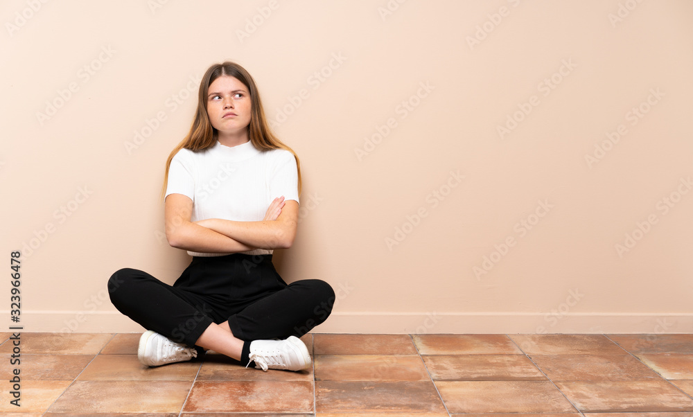 Ukrainian teenager girl sitting on the floor making doubts gesture while lifting the shoulders Ukrainian teenager girl sitting on the floor making doubts gesture while lifting the shoulders