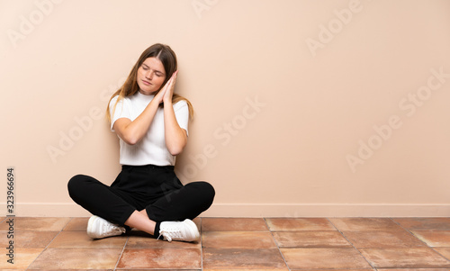 Ukrainian teenager girl sitting on the floor making sleep gesture in dorable expression