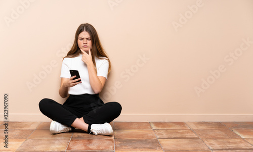 Ukrainian teenager girl sitting on the floor thinking and sending a message