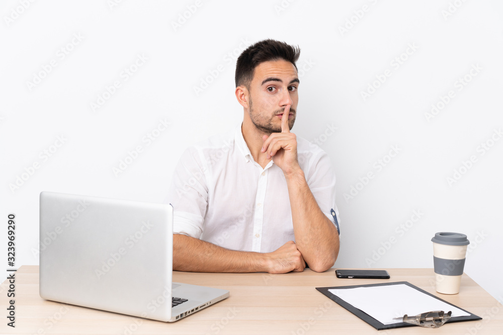 Young business man with a mobile phone in a workplace doing silence gesture Young business man with a mobile phone in a workplace doing silence gesture