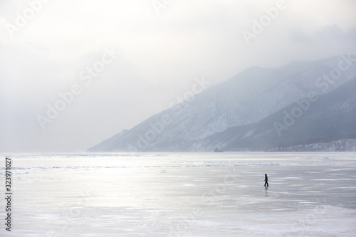 Woman walking on the frozen ice of lake Baikal on a windy day with a snow storm. Lake Baikal, Siberia, Russia.