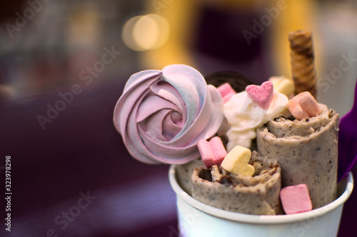 Handmade natural ice cream roll made from organic products. Healthy food concept. Ice cream from Thailand. Portion cold dessert decorated with meringue  marshmallows and wafer in paper cup.