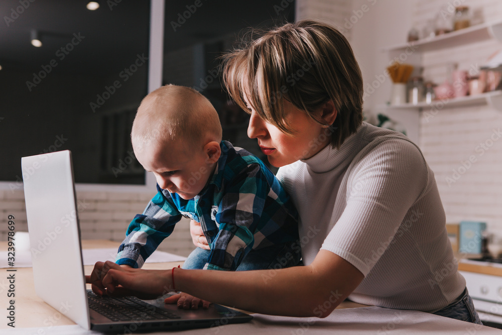 Beautiful business mom is using a laptop while spending time with her cute baby boy at home Beautiful business mom is using a laptop while spending time with her cute baby boy at home