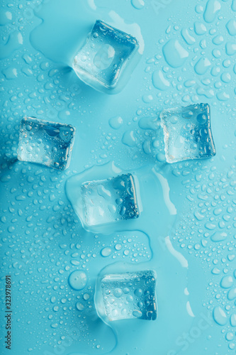 Ice cubes with water drops scattered on a blue background, top view.