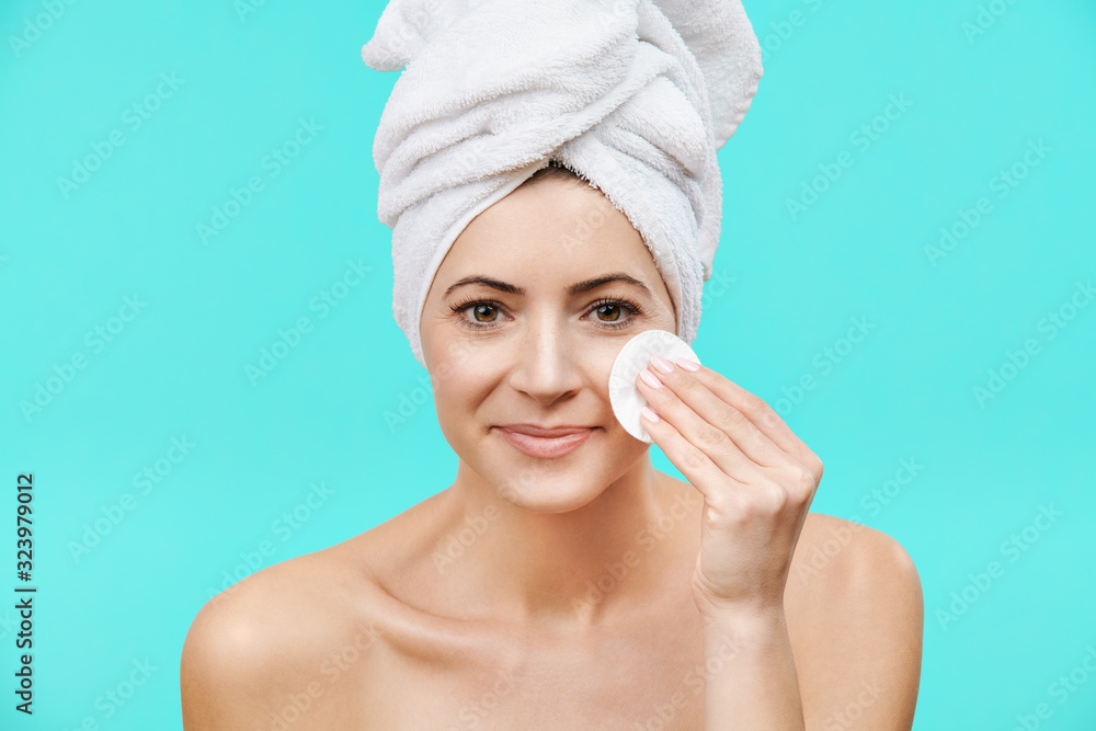 Smiling mid adult woman removing make up using a cotton pad. Photo of an attractive caucasian woman with healthy skin isolated on turquoise background. Beauty and Skincare concept. Smiling mid adult woman removing make up using a cotton pad. Photo of an attractive caucasian woman with healthy skin isolated on turquoise background. Beauty and Skincare concept.