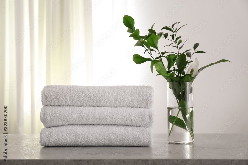 Fresh towels and green branches on light grey stone table in bathroom Fresh towels and green branches on light grey stone table in bathroom