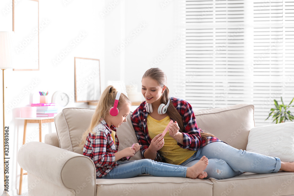 Happy mother and little daughter with headphones filing nails on sofa at home Happy mother and little daughter with headphones filing nails on sofa at home