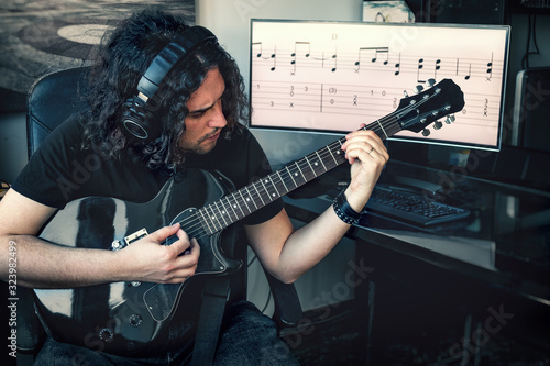 long haired rock composer musician man with headphones play electric guitar with musical score on screen background photo