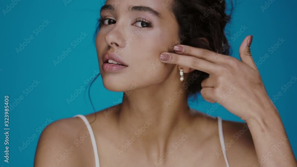 attractive woman runs her fingers on face and smiling to camera isolated on blue attractive woman runs her fingers on face and smiling to camera isolated on blue