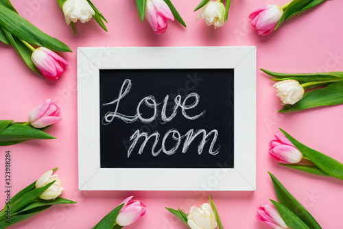Top view of tulips around chalkboard with love mom lettering on pink background