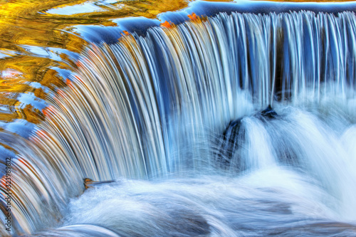 Bond Falls cascade captured with motion blur and illuminated with reflected color form sunlit autumn foliage, and blue sky overhead, Michigan's Upper Peninsula, USA