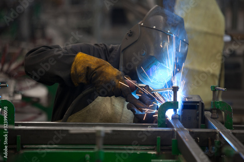 worker in mask, in the process of welding metal with bright light, smoke and sparks