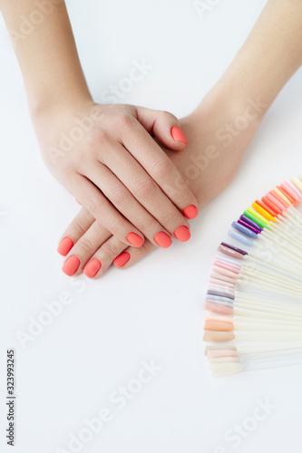 Beautiful female hands with trendy coral bright manicure and multicolor palette on the white background