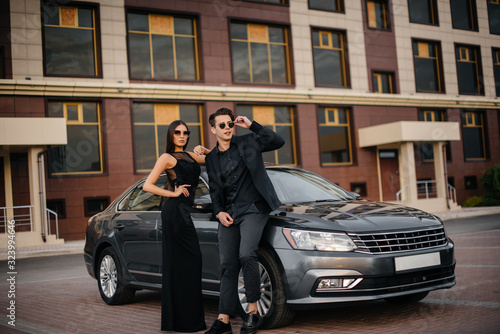 A young stylish couple in black stands near the car at sunset. Fashion and style © Andrii