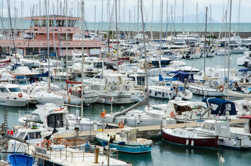 Boats and motorboats moored at the piers of a tourist port. In the background, the control tower of the port authority