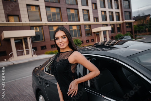 Stylish young girl stands near the car in a black dress. Business fashion and style © Andrii