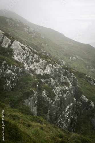 Irish cliff made of grey stones and green grass under a cloudy grey sky I