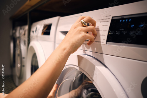 Close up girl turning on washing machine in self-service laundry