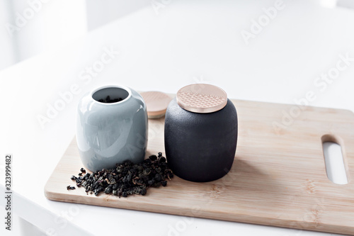 two teapots stand on a wooden board on a white table in a bright kitchen, next to which green tea is scattered