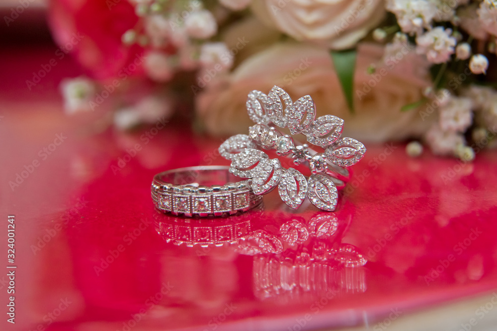White wedding rings . flower bouquet selective focuse .Two silver wedding rings red background . Romantic and lovely wedding , macro . Bride and groom with Engagement gold rings put on the red table . White wedding rings . flower bouquet selective focuse .Two silver wedding rings red background . Romantic and lovely wedding , macro . Bride and groom with Engagement gold rings put on the red table .
